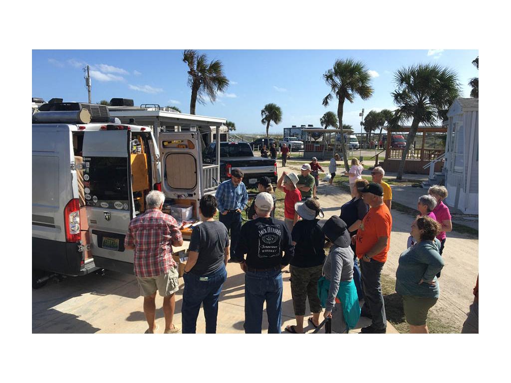 Scott teaching lesson to RV group standing in circle around silver Travato.