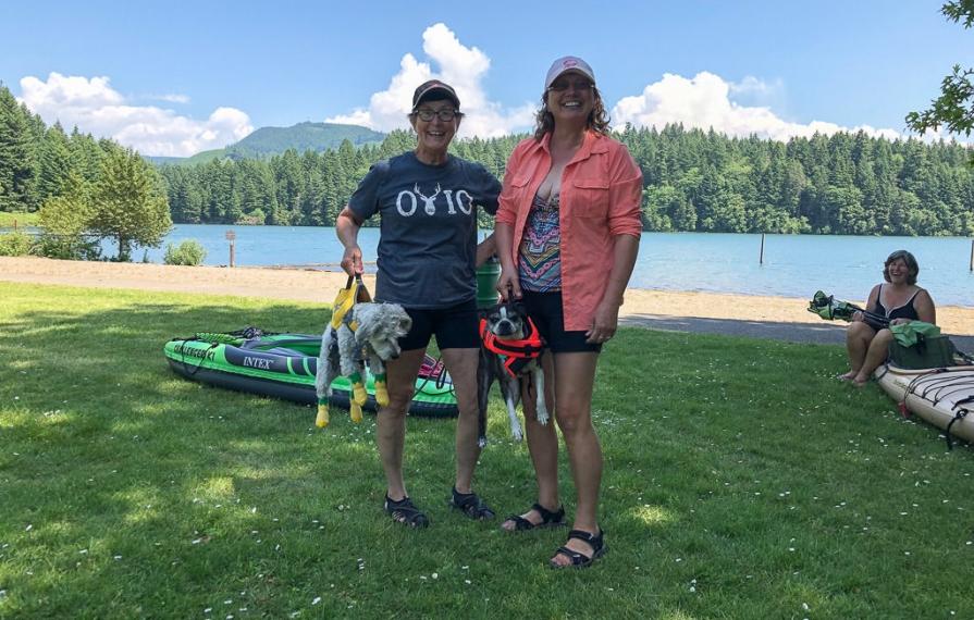 Two people showing off their dogs wearing life jackets