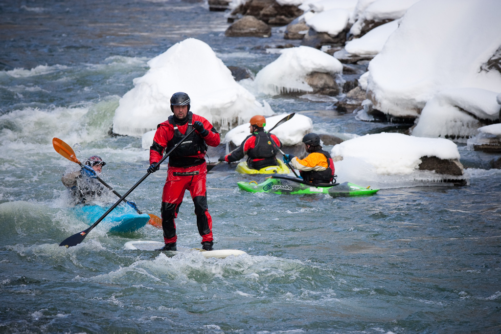 Kayakers and a paddle boarder going down the rough waters of the river.
