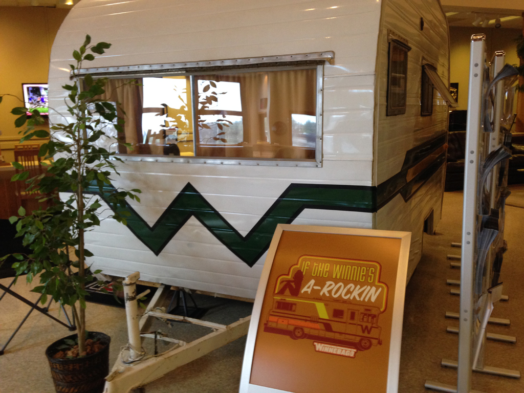 Vintage Winnebago towable with sign outside that says, "If the Winnie's A-Rockin."