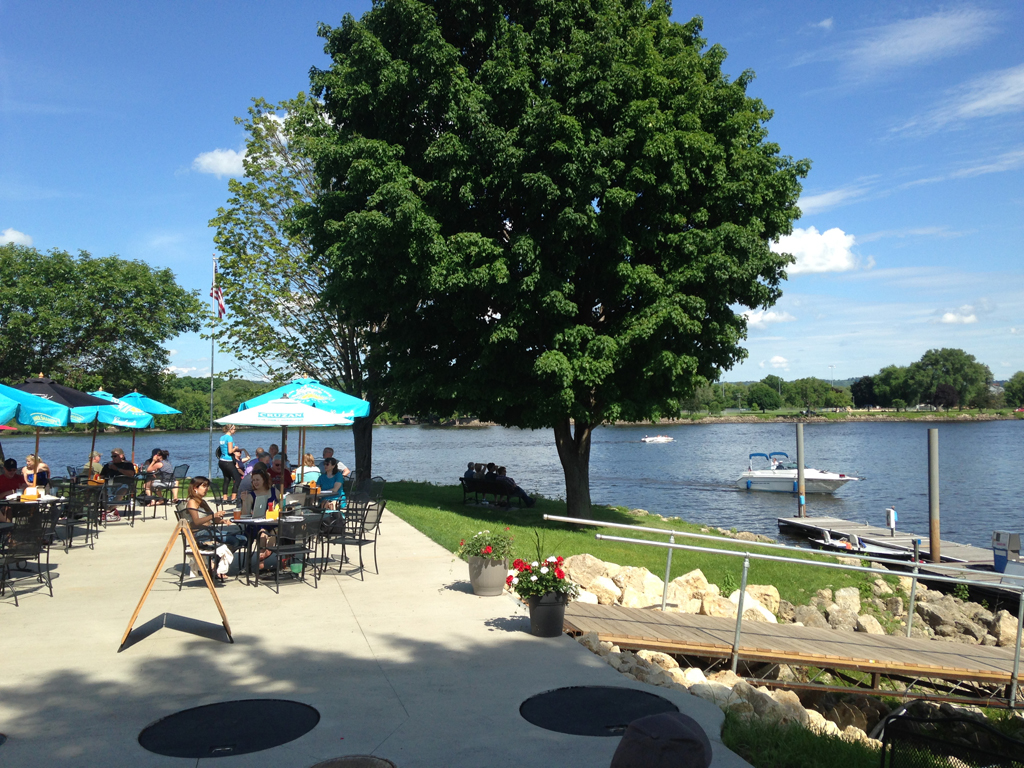 People dining at tables along the water at a restaurant.