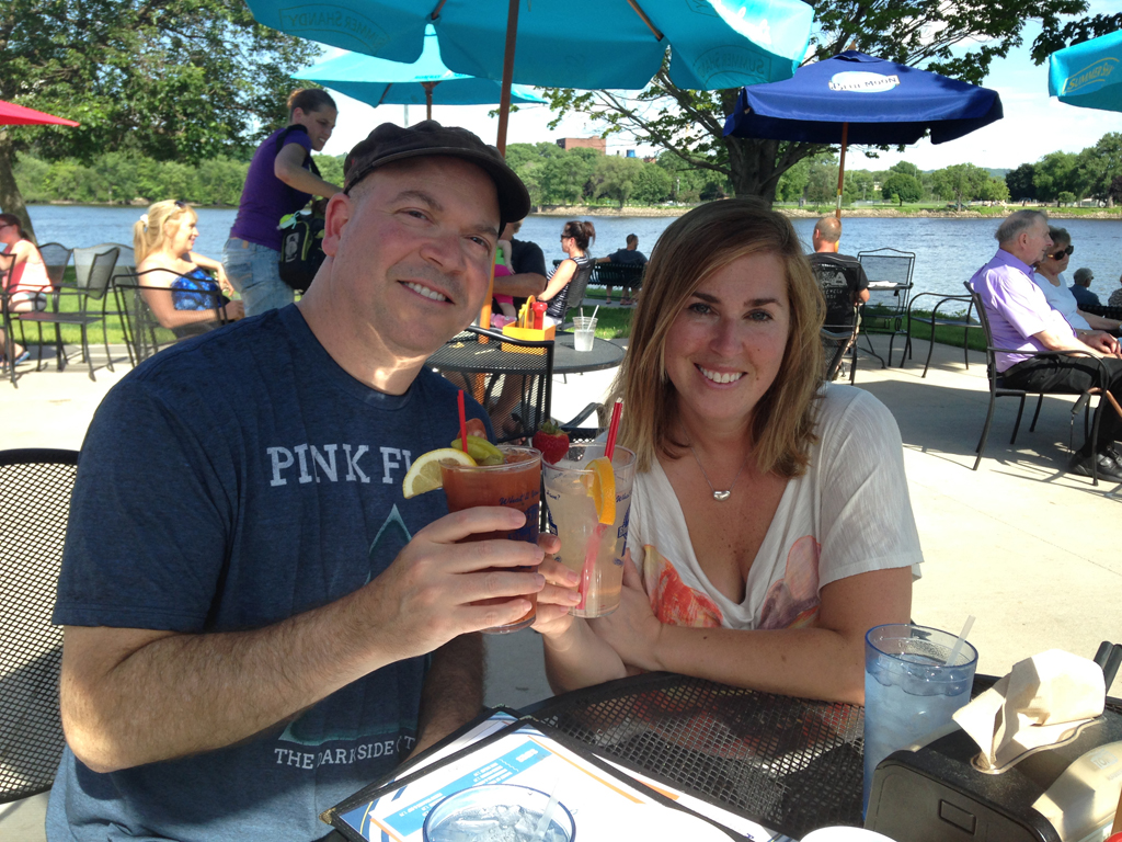 Couple at table outside along the water holding their drinks.
