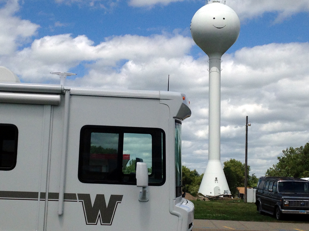 Winnebago motorhome parked in front of smiley face water tower.