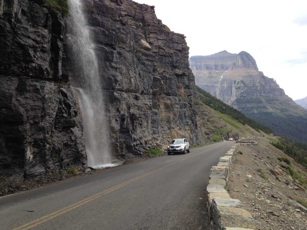 Waterfall down the side of a rocky cliff right along a narrow road.