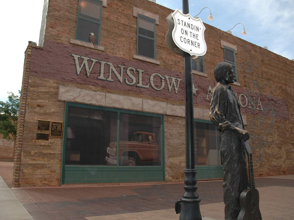 Statue on a corner standing under sign on light post that reads "Standin' on the Corner."