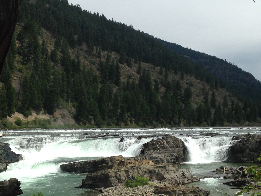 Kootenai Falls at the base of a tree covered hillside.