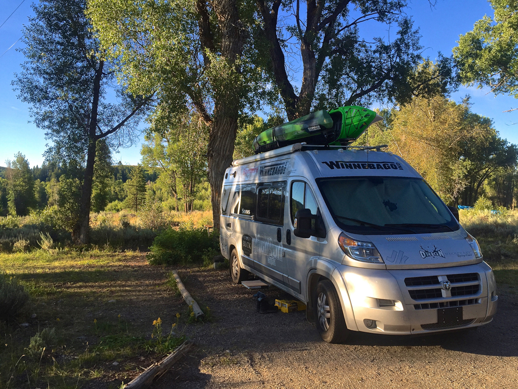 Winnebago Travato parked on street with gear attached to top and backside.