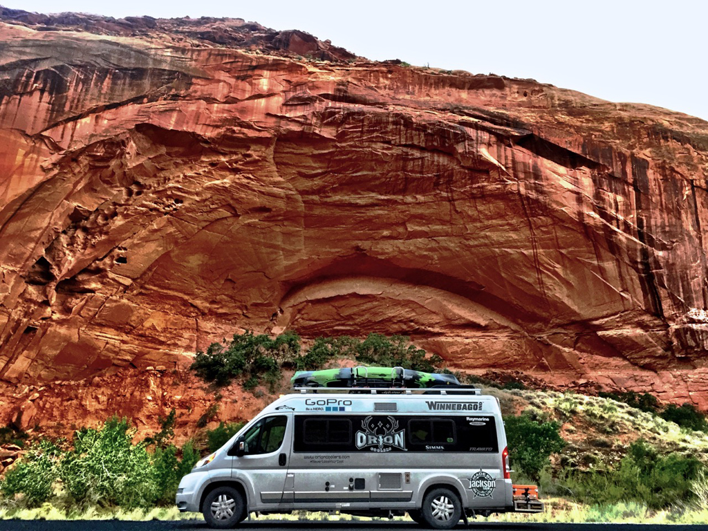 Winnebago Travato parked beneath red rock canyon.