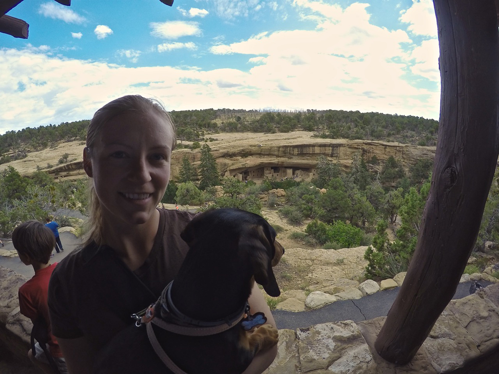 Woman holding her dog with the ancient buildings in the background.
