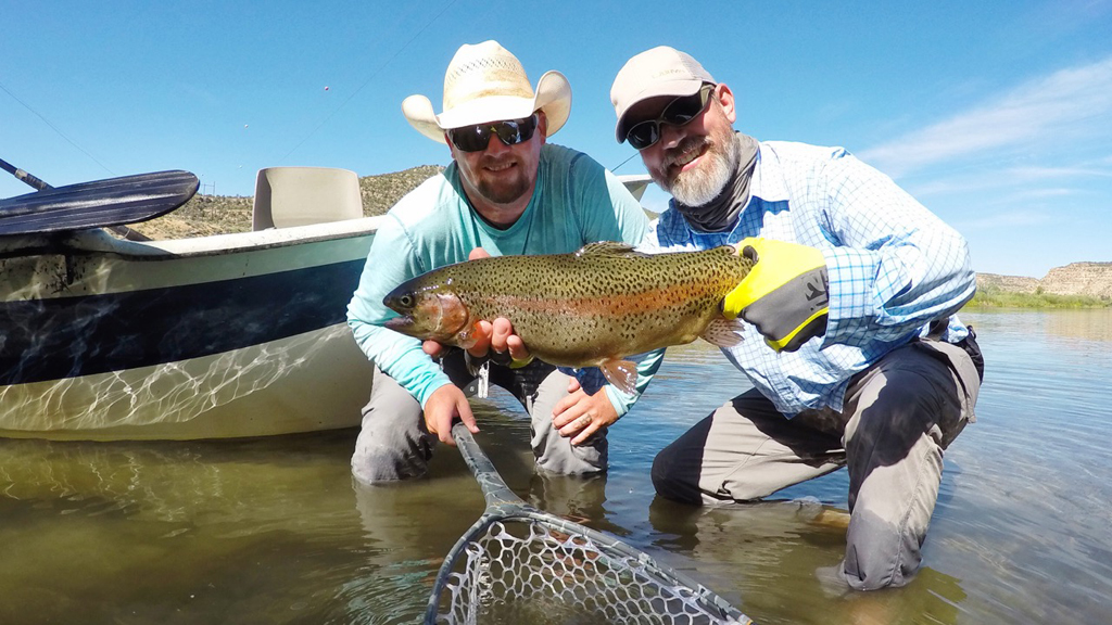 Two people kneeling in the water with one man holding a fish.