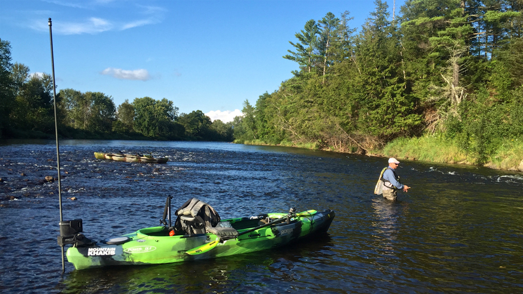 Man wading in water fishing with kayak floating nearby.
