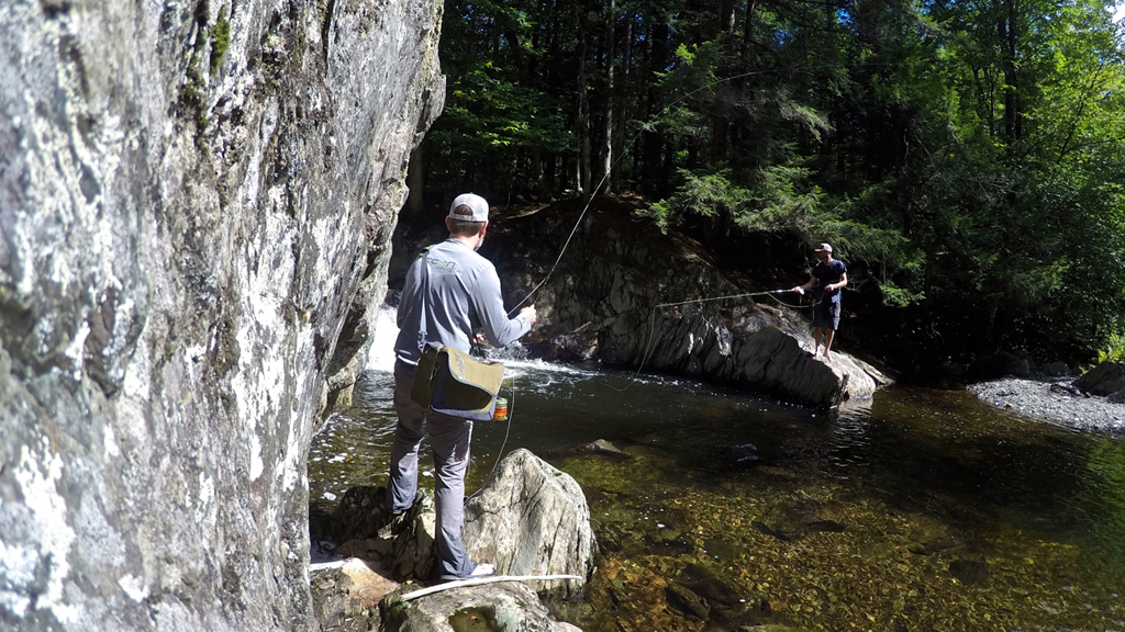 Man fly fishing from rocks next to the water.