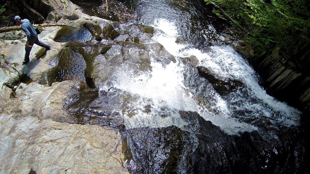 Man walking next to small waterfall.