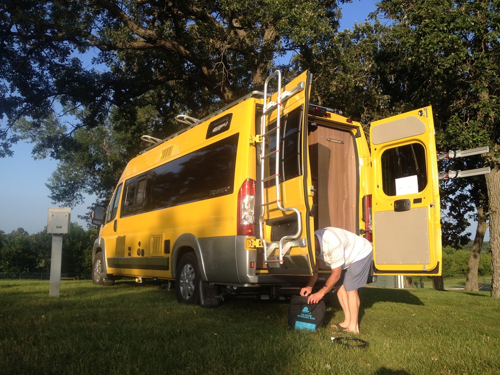 Person standing at the back of their Winnebago Travato with the back doors open..
