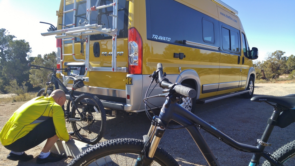 Man prepping bikes at the back of Winnebago Travato.