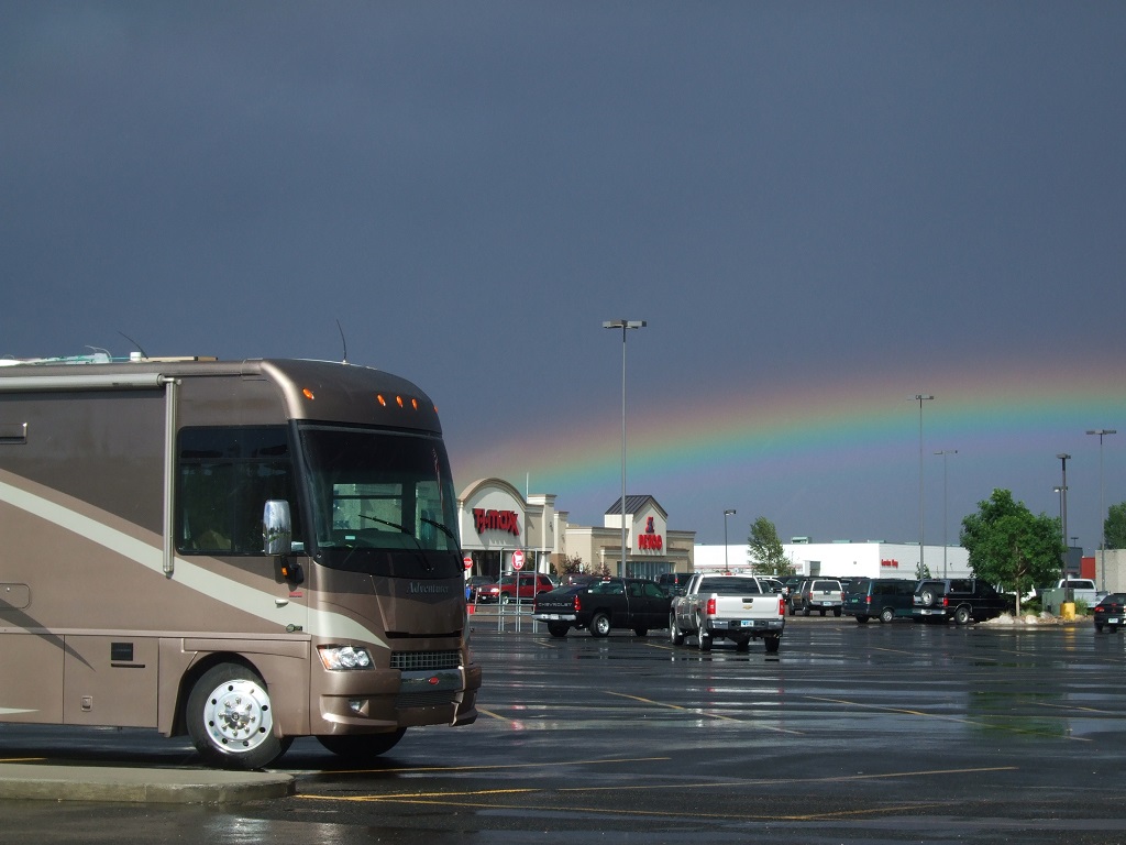 Winnebago parked in parking lot, with rainbow overhead.