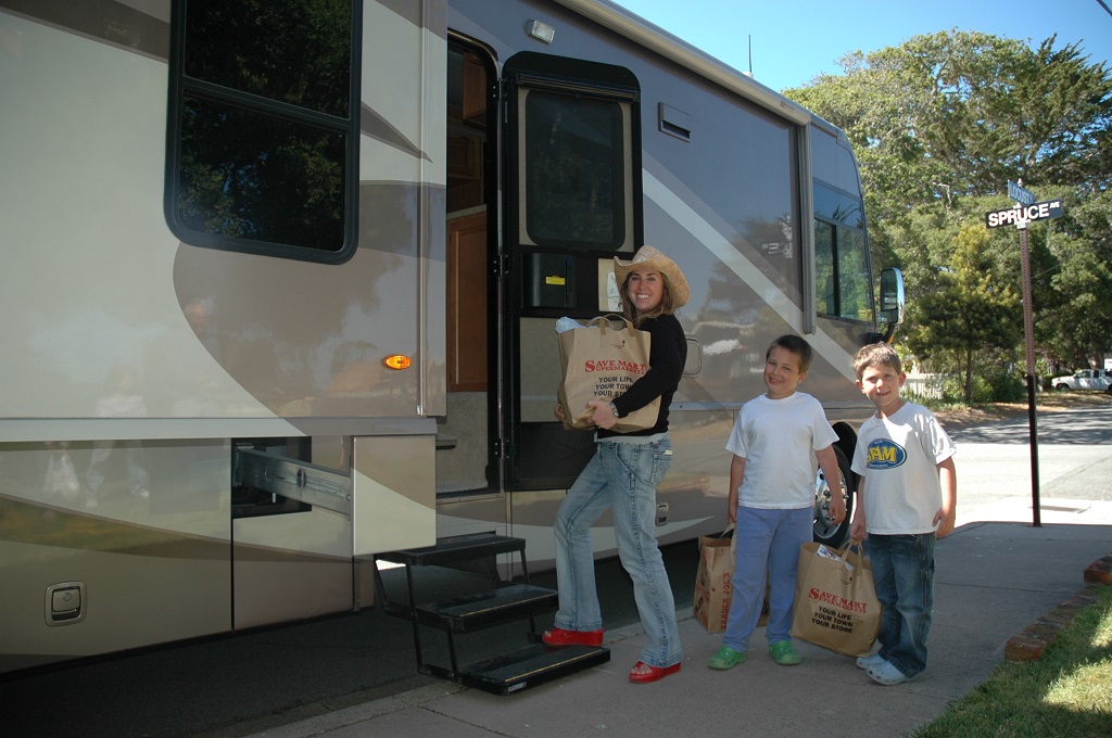 Woman and toy boys heading into their RV with grocery bags.