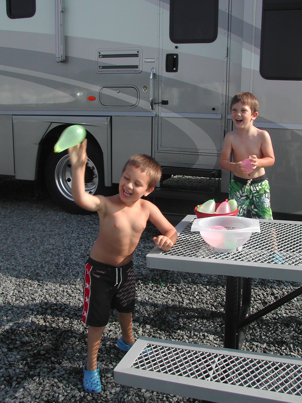 Two boys playing with water balloons outside motorhome.