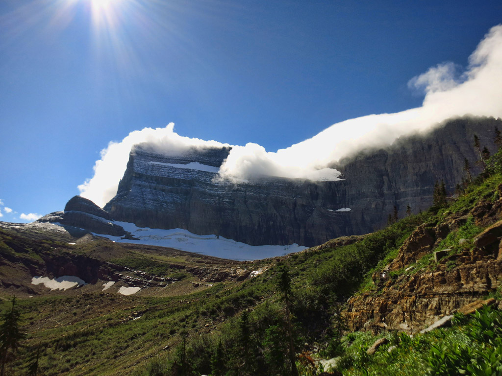 Mountains and glacier with clouds that seem to be resting at the top of them.