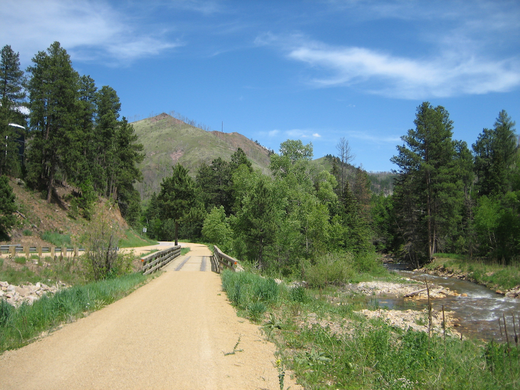Path along river through trees leading up to hillsides.