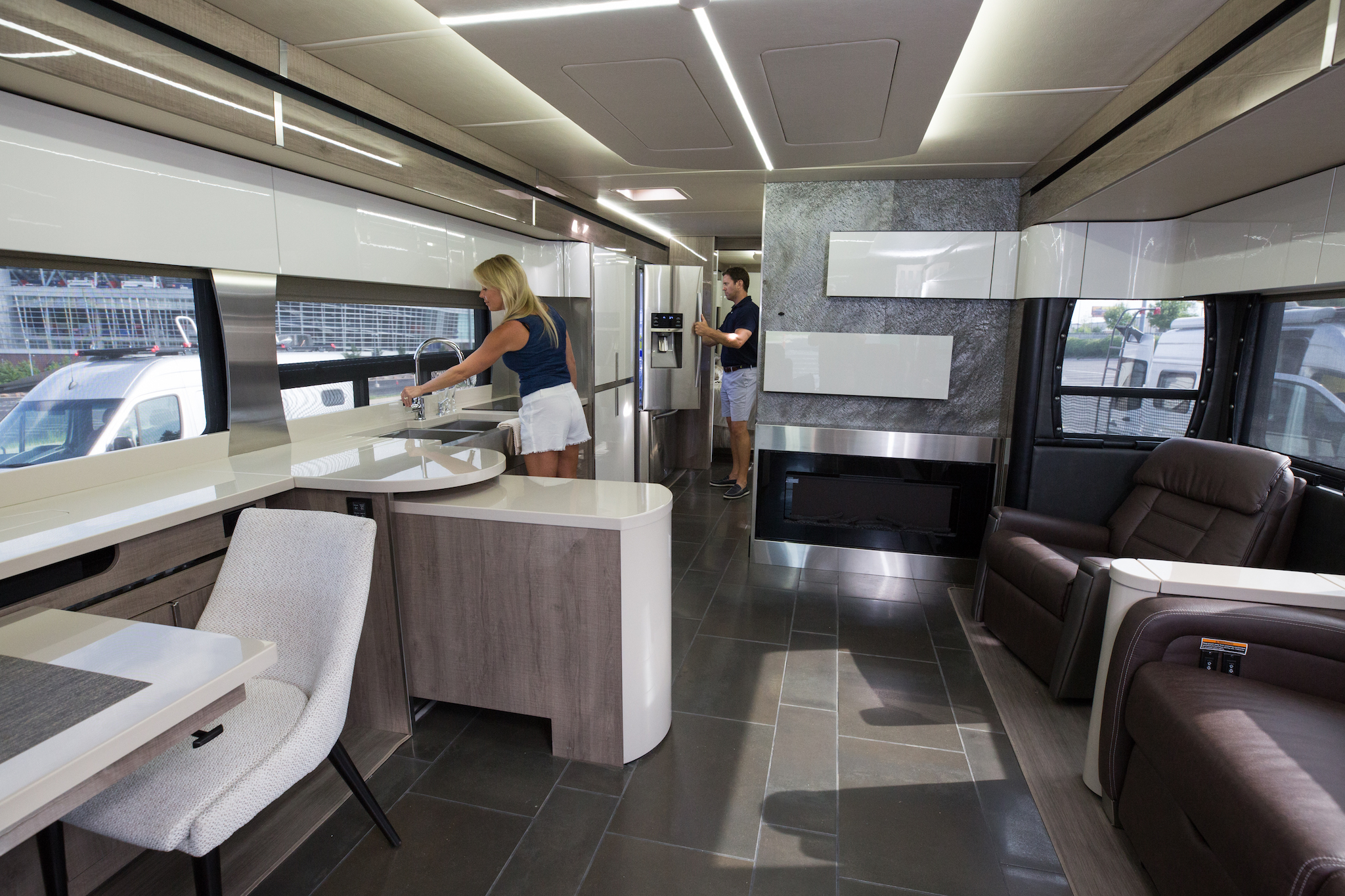 Woman at the kitchen sink and man looking in the fridge of a modern Winnebago Horizon.