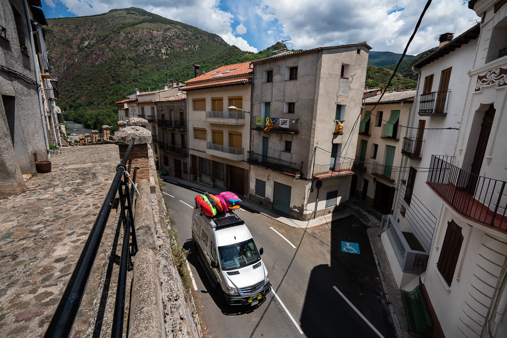 Winnebago Revel driving on narrow road through a town.